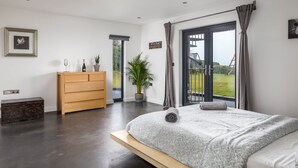 Un dormitorio moderno con una cama grande, un aparador de madera, una planta en maceta y vistas al exterior a través de una puerta corrediza de vidrio.