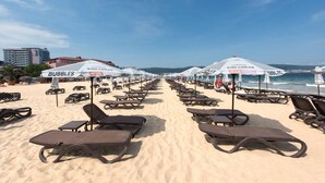 Uma praia com fileiras de espreguiçadeiras e guarda-sóis identificados como 'Bubbles' e 'Wine Cooler'.