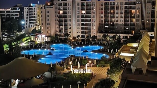 Vista noturna de um hotel com várias piscinas, incluindo uma piscina central ampla, e uma área ajardinada com guarda-sóis.