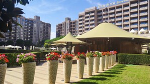 Hotel com fachada moderna, áreas de estar ao ar livre e jardineiras com flores.