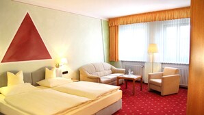 Ein Hotelzimmer mit einem Bett, zwei Sesseln, einem kleinen Tisch und einer Lampe.