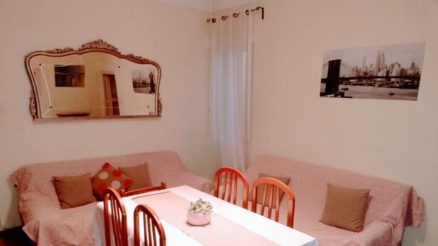 Una habitación acogedora con una mesa de comedor, sillas, un sofá, un espejo y un cuadro de un paisaje urbano.