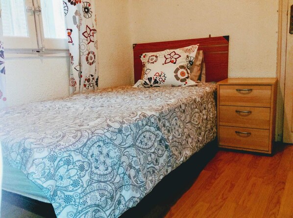 Ein kleines, aufgeräumtes Schlafzimmer mit einem Einzelbett, einem Nachttisch und einer hölzernen Kommode.