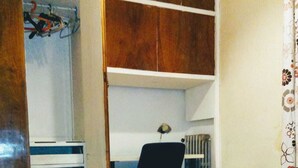 Un dormitorio con una cama, un escritorio y una silla. Hay un armario con barra para colgar y un aparador.