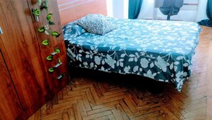 Un dormitorio con suelo de madera en espiga, una cama con colcha estampada, un armario de madera con pomos verdes y una pequeña planta en la pared.