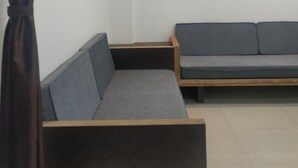 A modern room with a dark wooden bench, a grey sofa, and a skylight ceiling. - RP Studio Rooms (Igatpuri)