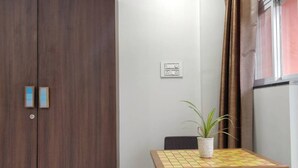 A room with a wooden wardrobe, a table with a potted plant, and a window with curtains. - RP Studio Rooms (Igatpuri)