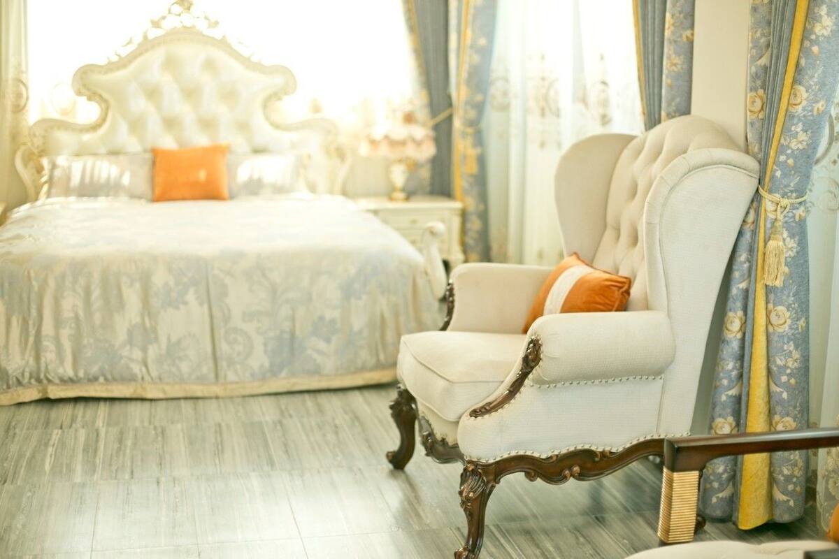 A bedroom with a large bed, ornate headboard, and a plush armchair with a cushion.