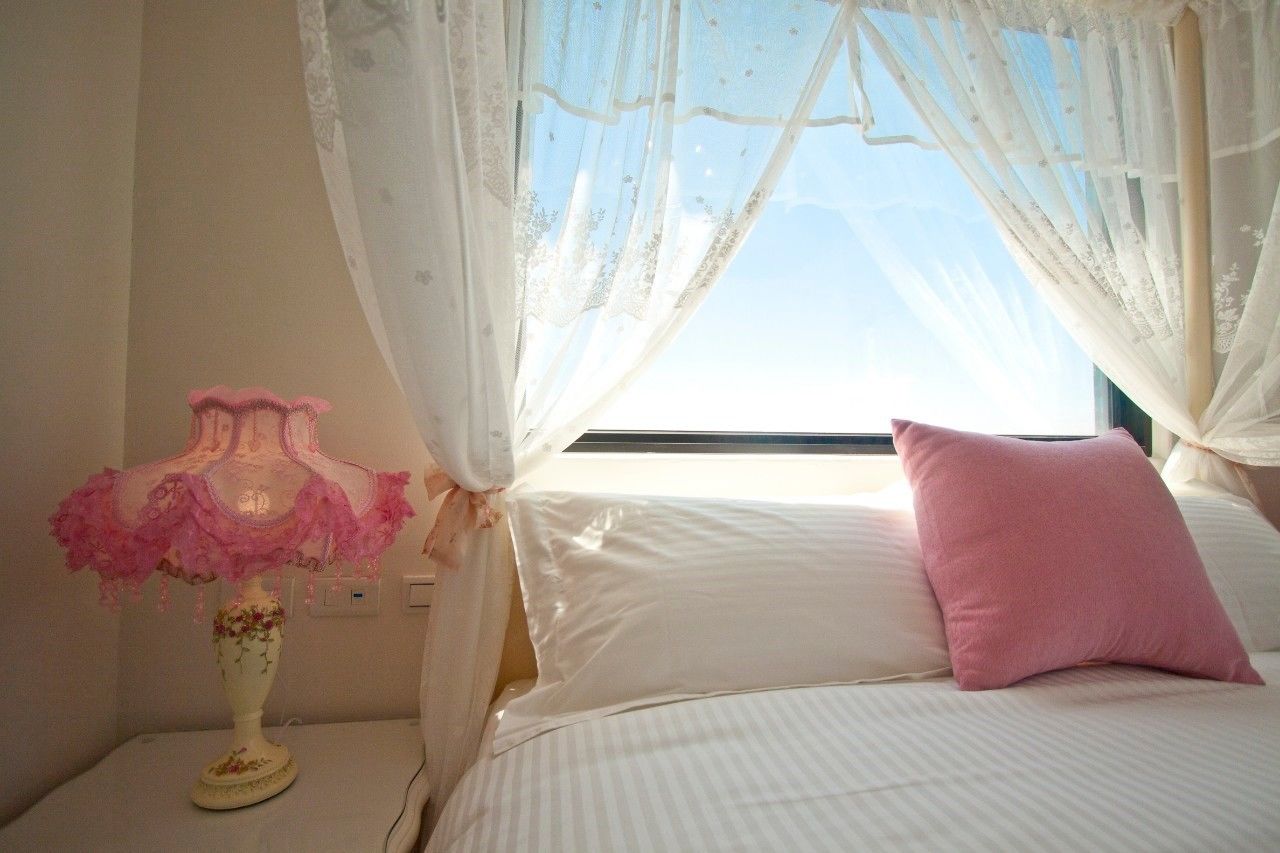 A bedroom with a bed, a nightstand, a lamp, and sheer curtains.