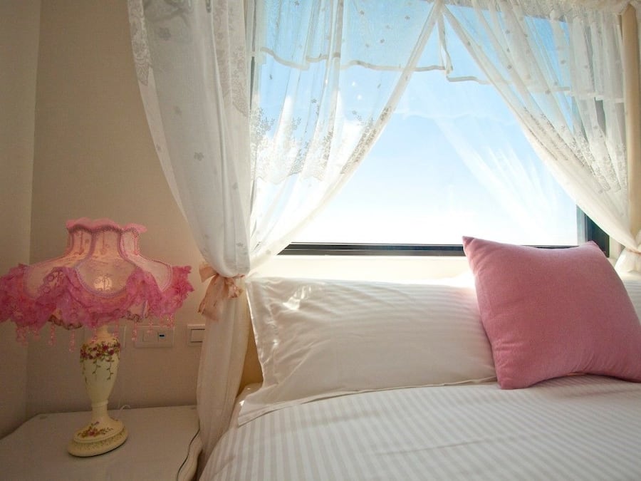 A bedroom with a bed, a nightstand, a lamp, and sheer curtains.