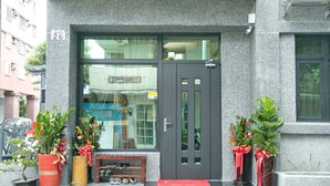 Ein Gebäudeeingang mit einer dunklen Tür, einer Bank und Topfpflanzen.