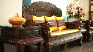 Ein traditionelles Sofa aus Holz mit aufwendigen Schnitzereien, ein passendes Holztablett mit dekorativem Deckel und eine Vase mit Blumen.