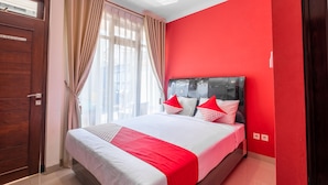 A hotel room with a large bed, red walls, and a wooden door. - OYO Collection O 1032 Rahayu Residence Syariah (West Cirebon)