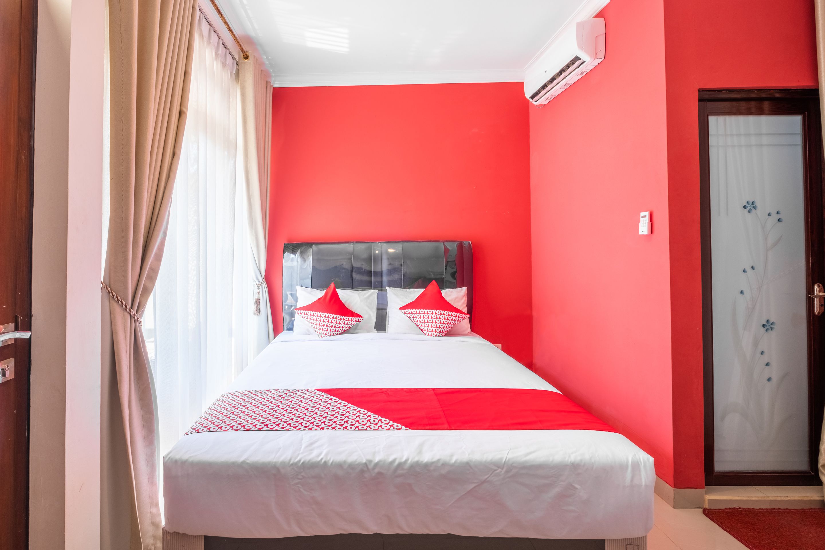 Habitación de hotel con una pared de acento roja, una cama con ropa de cama blanca y roja, y una puerta con un diseño floral.