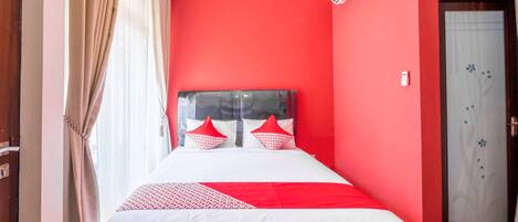 A hotel room with a red accent wall, a bed with white and red bedding, and a door with a floral design.