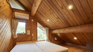 A wooden cabin bedroom with a large bed, a window, and an air conditioning unit. - Family Cottage NOTOIE (Shika)
