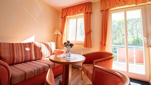 Une pièce comprenant un canapé, un fauteuil, une table avec un vase et une fenêtre avec des rideaux.