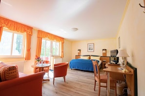 Habitación de hotel con cama, escritorio, silla, mesa y ventana con cortinas.