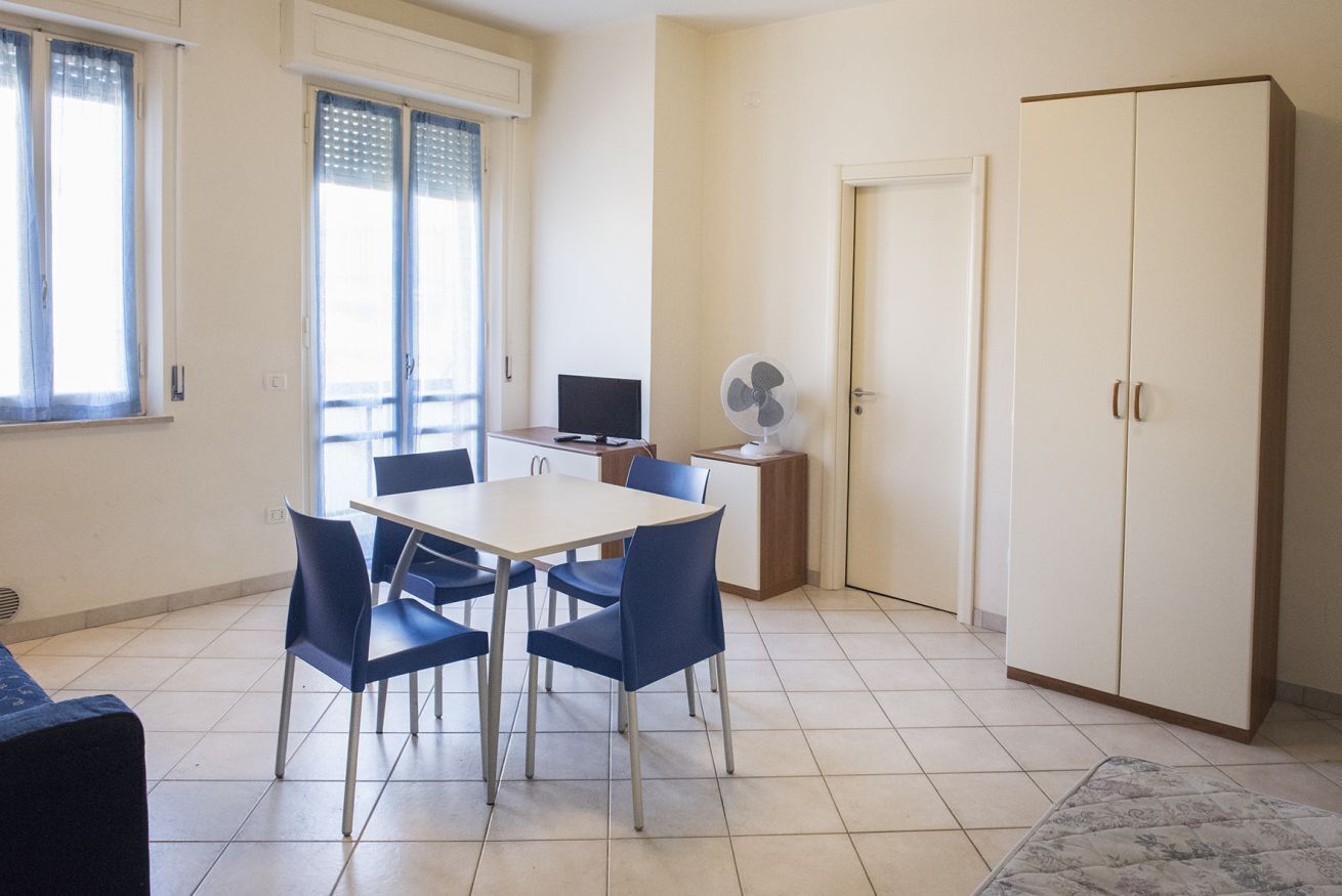 A room with a dining table, chairs, a TV, a fan, and a wardrobe.