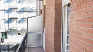 En smal balkon med gelænder i metal, en murstensvæg og et vindue.