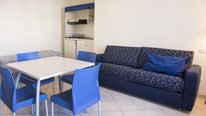 En kompakt bolig med tekøkken, spisebord med stole og sofa med mønstrede puder.