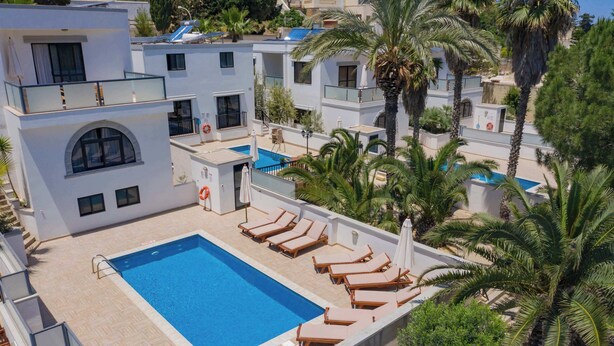 A rooftop pool area with sun loungers, a swimming pool, and a view of modern buildings.