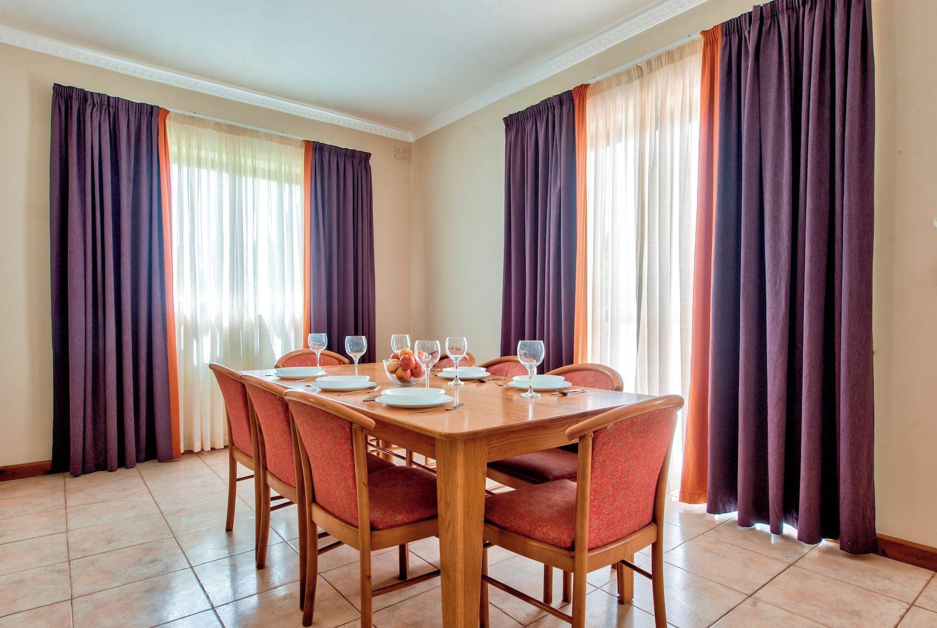 A dining area with a wooden table set for four, surrounded by red upholstered chairs.