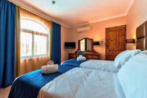 Ein Hotelzimmer mit zwei Betten, einem Schreibtisch mit Stuhl, einem Spiegel, einer Klimaanlage und einer Holztür.