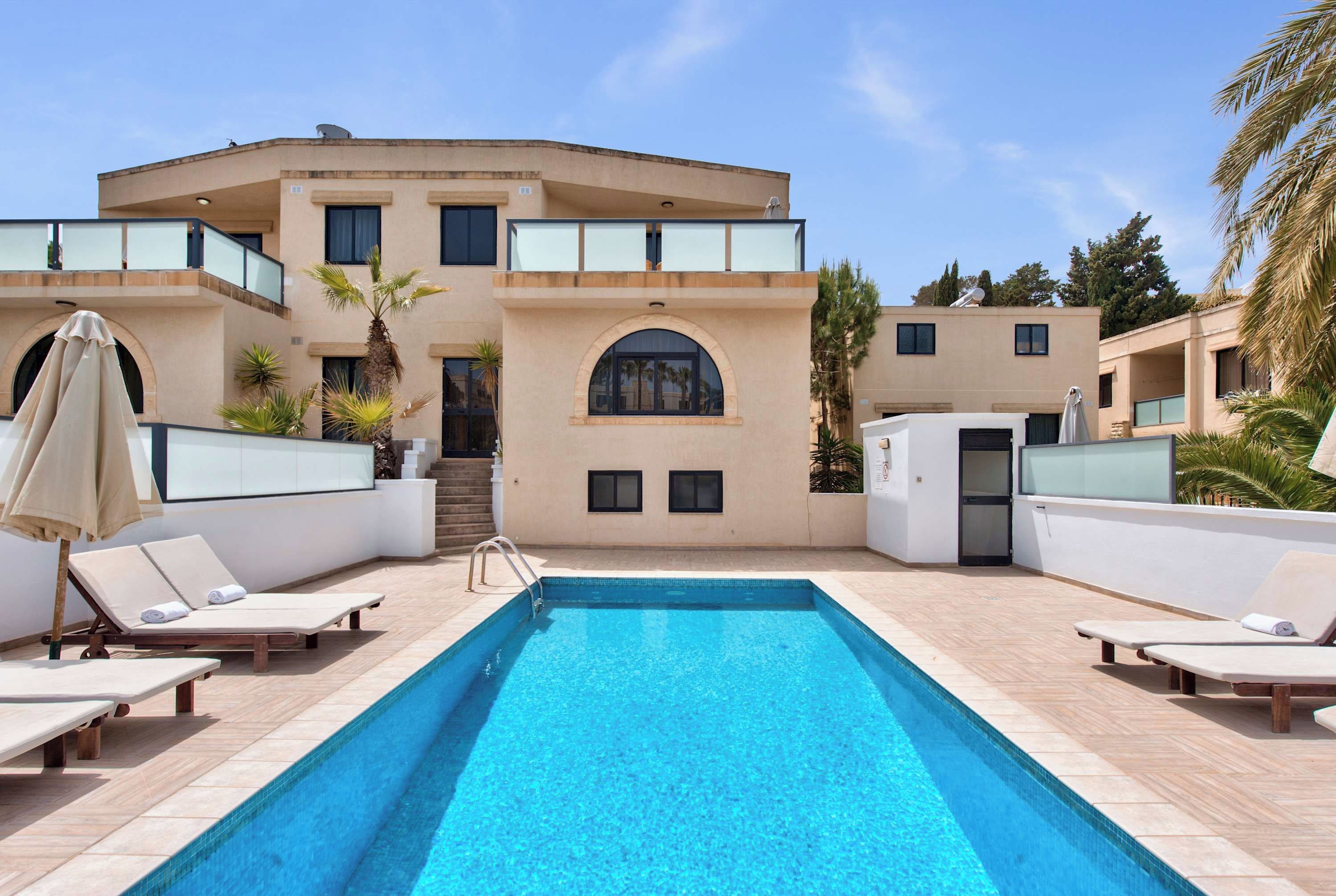 Un bâtiment moderne doté d’une piscine, de chaises longues et de palmiers.