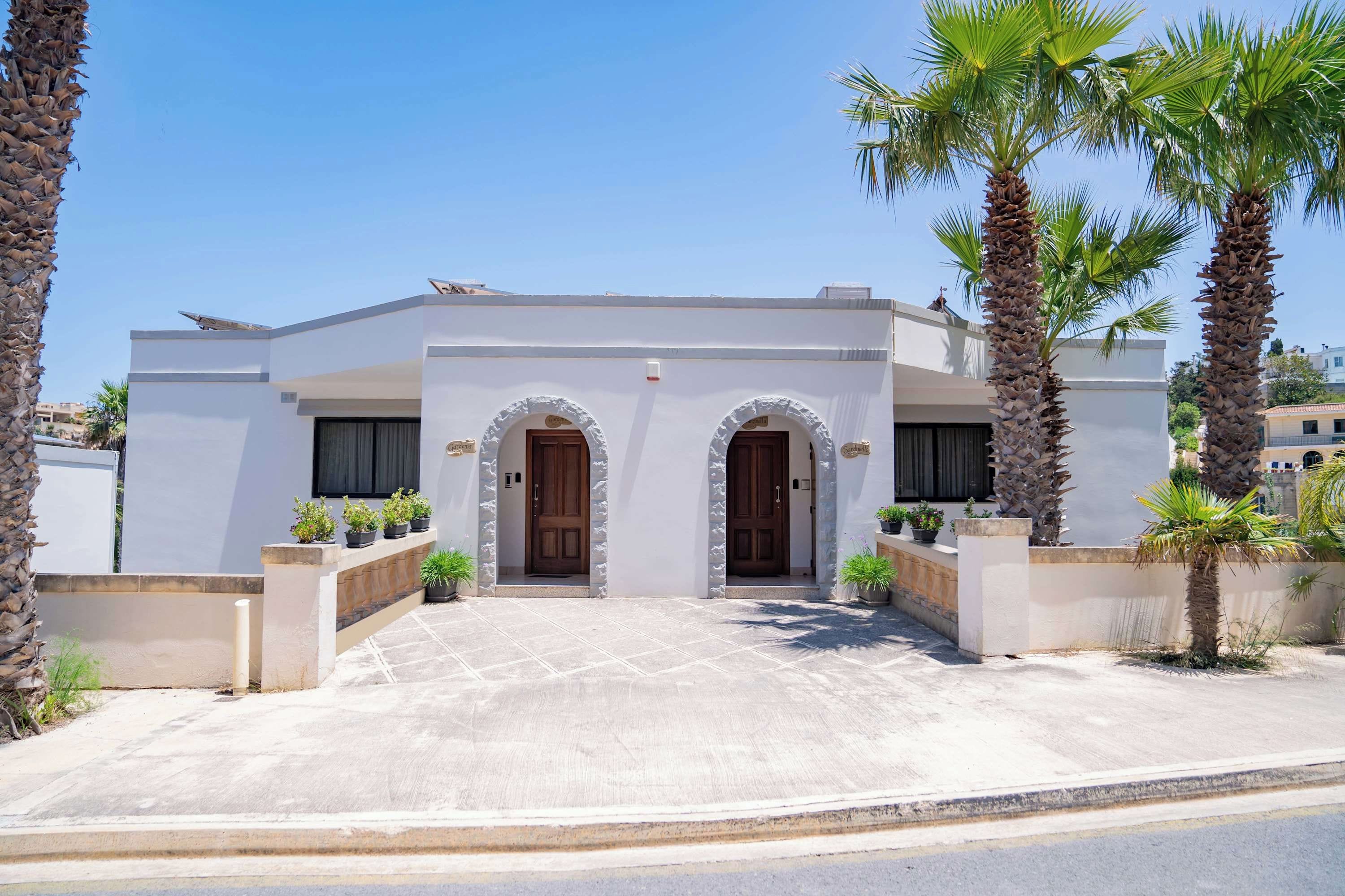 A modern building with a white facade, two arched doorways, and a paved entrance.