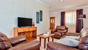 A living room with leather sofas, a wooden coffee table, a flat-screen TV, and decorative wall art.