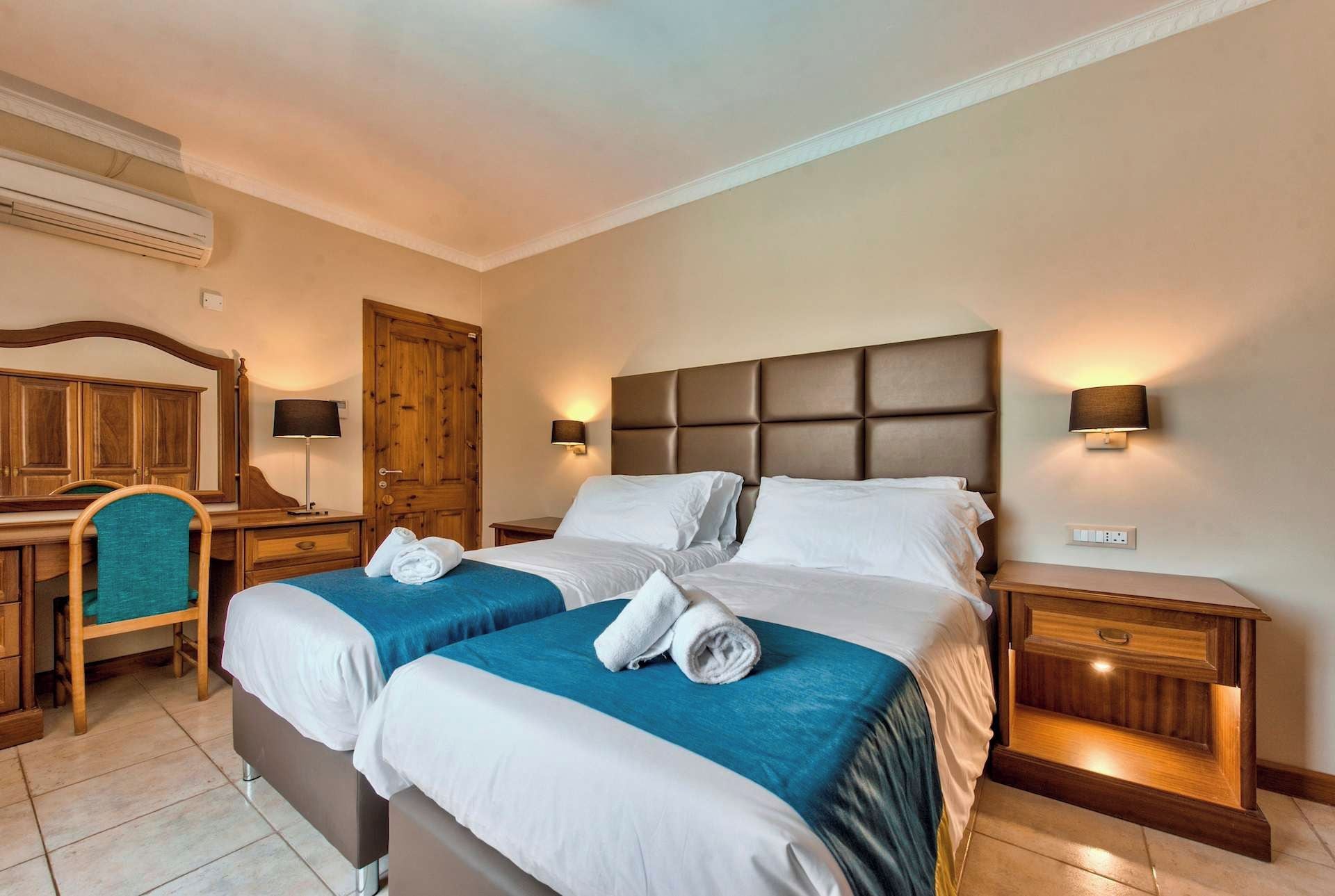 Une chambre d’hôtel avec deux lits, une armoire en bois, un bureau avec une chaise et un miroir.