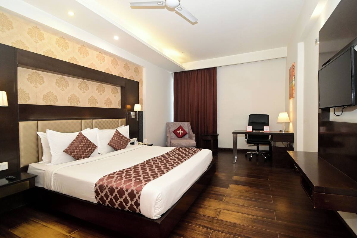Une chambre d’hôtel avec un grand lit, un bureau, une chaise, une télévision et un ventilateur de plafond.