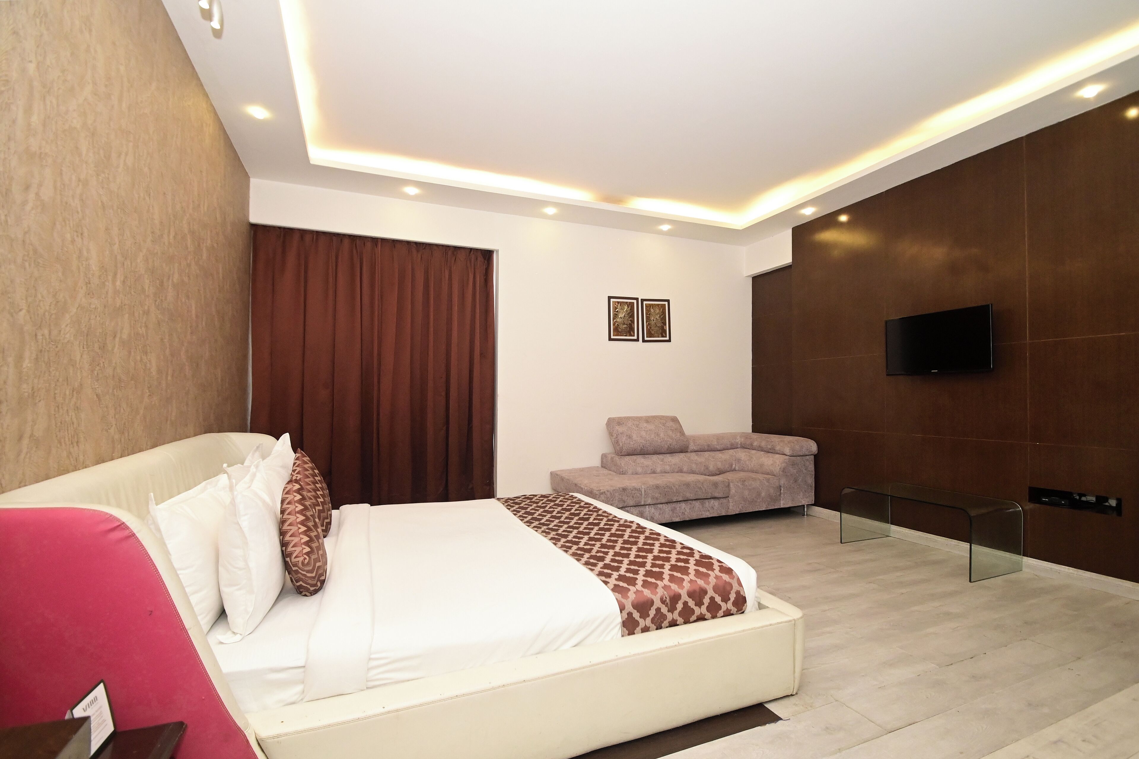 A modern hotel room with a bed, a sofa, a TV, and a glass bench.