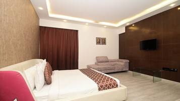 A modern hotel room with a bed, a sofa, a TV, and a glass bench.
