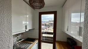 A compact kitchen with white cabinets, a wooden countertop, a built-in dishwasher, and a window with a view of a snowy mountain town.