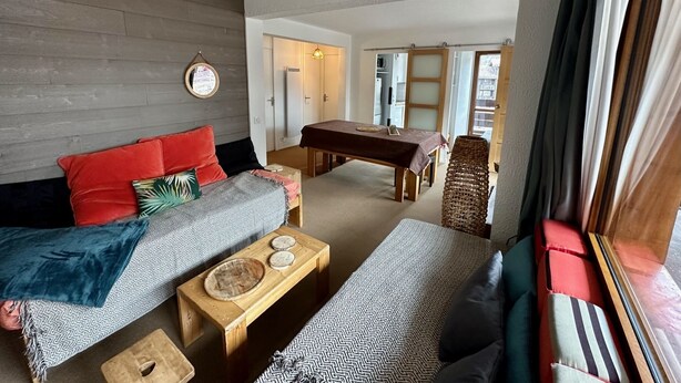 A cozy living room with a sofa, a dining table, and a window with curtains.