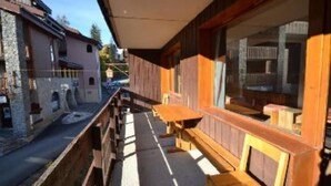 A wooden balcony with a table and benches, overlooking a street with stone buildings.