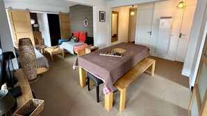 A cozy bedroom with a bed, bedside tables, a bench, a desk, and a chair. There is a wardrobe, a mirror, and a door with a heater.