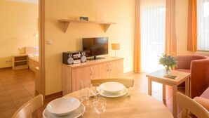 A dining area with a wooden table set for two, a television on a wooden cabinet, and a red armchair. - Vacation apartment WE12 - Holiday apartments at the sports field (Sellin)
