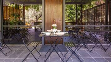 An outdoor patio with a wooden door, tables, chairs, and a vase with flowers.