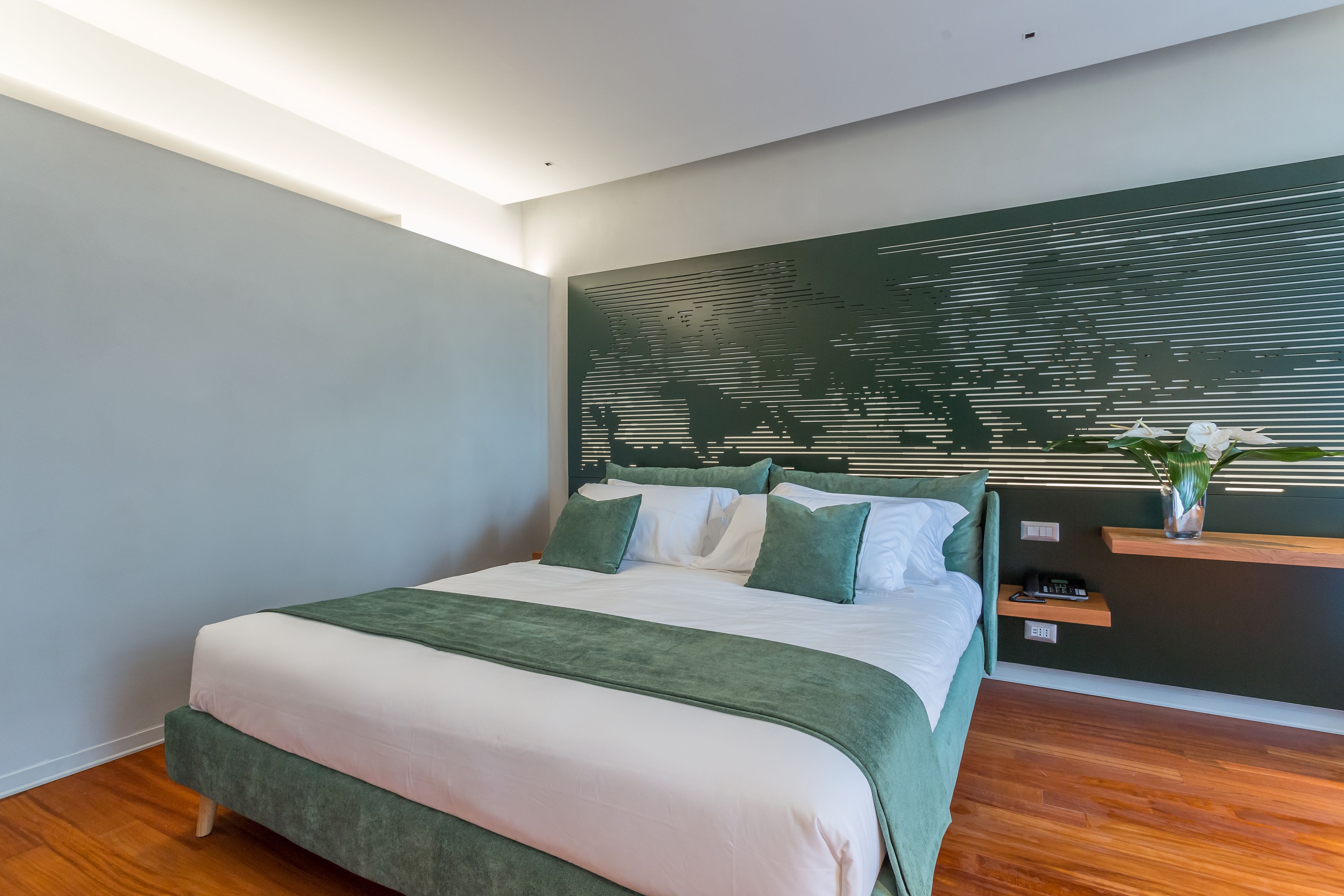 Une chambre moderne avec un grand lit, une tête de lit ornée d’une carte du monde, une table de chevet avec une plante et un plancher en bois.