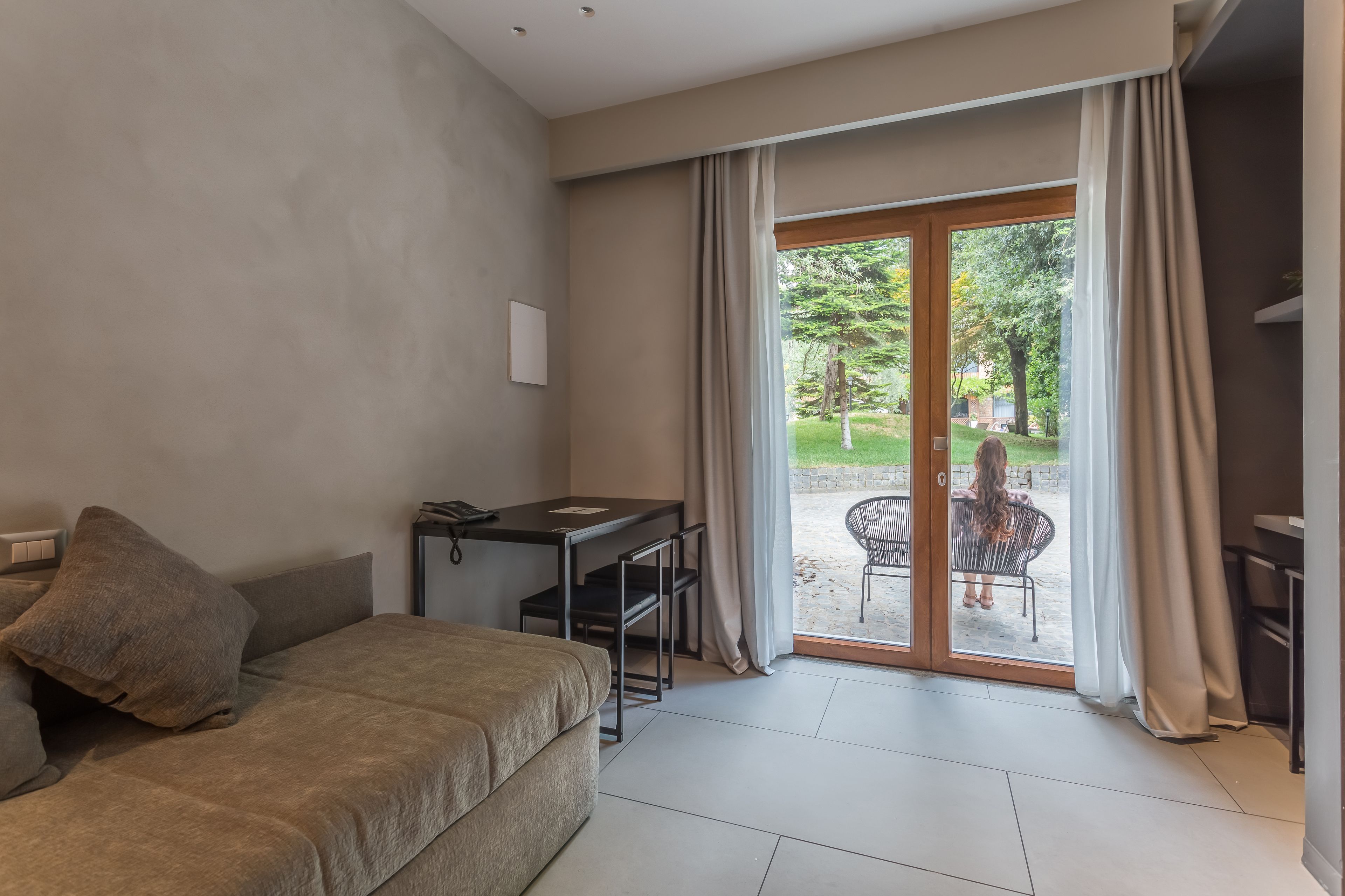 Una habitación moderna con sofá, escritorio y vista a un jardín a través de una puerta corredera.