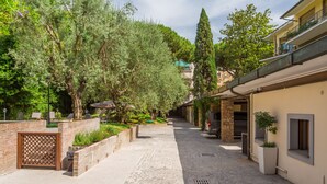 A cobblestone pathway flanked by trees and a brick wall with a lattice gate. - Fauno Urban Resort (Rome)