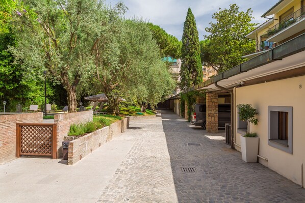 A cobblestone pathway flanked by trees and a brick wall with a lattice gate. - Fauno Urban Resort (Rome)