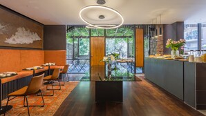 A modern dining area with a glass-top table, wooden chairs, and a view of greenery through large windows. - Fauno Urban Resort (Rome)