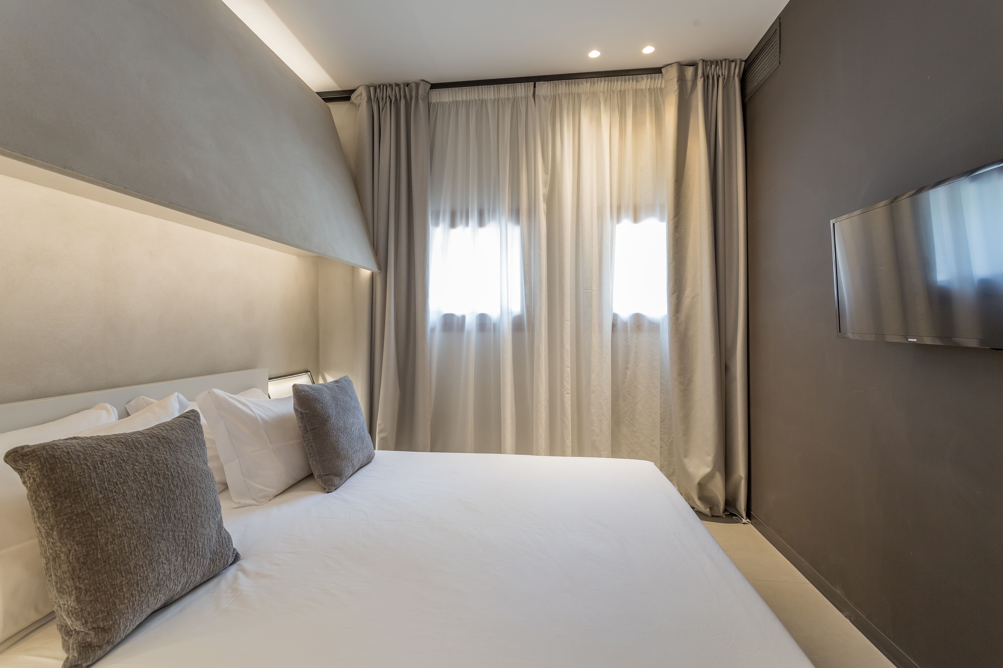 A modern hotel room with a large bed, two pillows, a flat-screen TV, and a window with curtains.