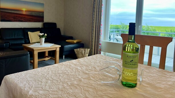 A hotel room with a bed, a table, a bottle of wine, and a view of the outdoors. - N19K (BC.a5) - Stranddomicil Steiner (Büsum)
