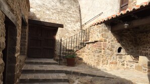 Una escalera de piedra que lleva a una puerta de madera, con una planta en maceta en los escalones y un muro de piedra con un ventanal pequeño.