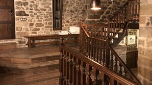 Una habitación con paredes de piedra, una escalera de madera, un banco y una lámpara colgante.